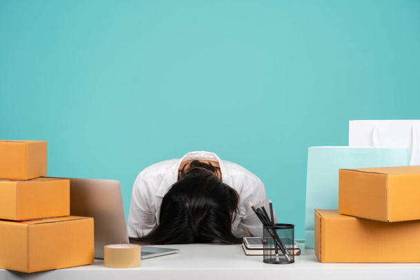 Cansado asiático mulher dormir colocou a cabeça para baixo em branco escritório mesa com pc laptop e caixa de papelão isolado em pastel verde fundo estúdio - Foto, Imagem