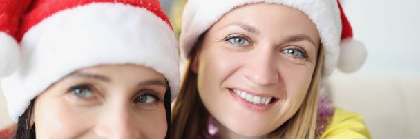 Portrait of smiling girls taking selfie to keep memory, cheerful friends or sisters in santa claus hats at home, ready to meet new year, wear festive outfits. Christmas, family, bff, fun concept - Фото, изображение