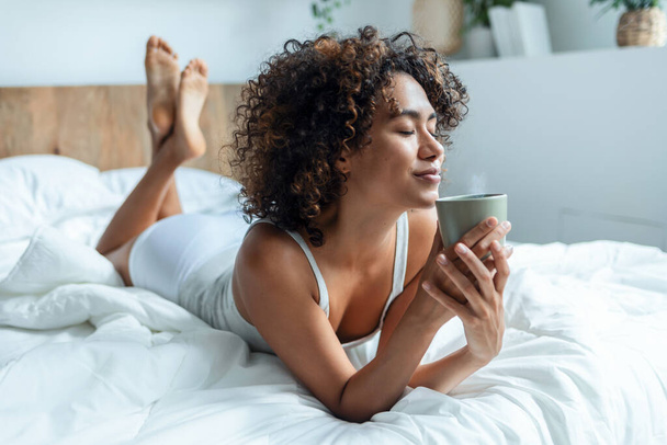Shot of beautiful woman drinking a cup of coffee while staying on the bed.  - Valokuva, kuva