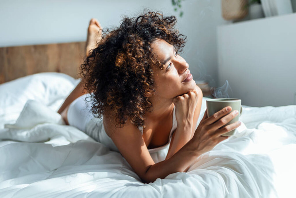 Shot of beautiful woman drinking a cup of coffee while staying on the bed.  - Foto, Imagem