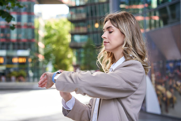 Close up portrait of businesswoman looking at her digital watch while waiting for someone outside. Corporate woman reading message on her wrist device. - Foto, Bild