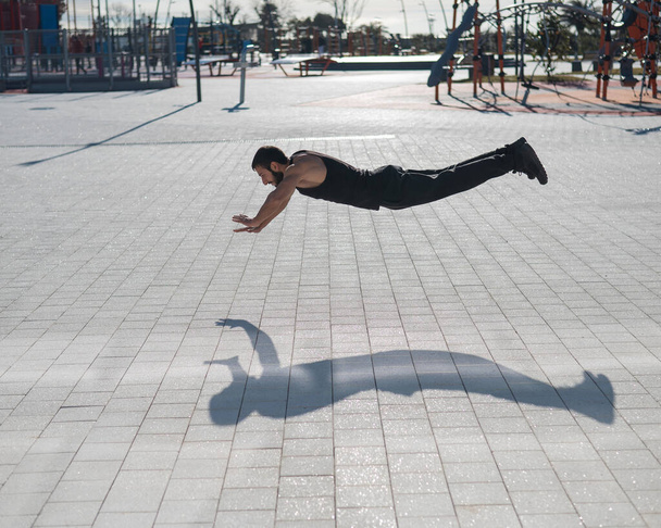 A man in black sportswear jumps doing push-ups in the park - Photo, Image