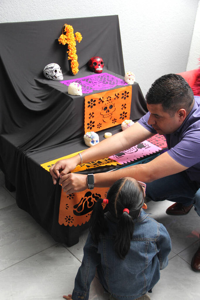 Mexican dad and daughter put the altar and offering of the Day of the Dead in their house for their deceased relatives part of the tradition and culture of Mexico - Photo, Image