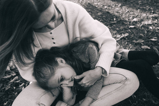 Anya és lánya az őszi parkban. Boldog arcok. Különleges életmód képfeldolgozás. Ül a füvön és sárgás leveleket. Boldog pillanatok. - Fotó, kép