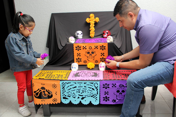 Mexikanische Väter und Töchter stellen den Altar und die Opfergabe des Tages der Toten in ihr Haus für ihre verstorbenen Verwandten, die Teil der Tradition und Kultur Mexikos sind - Foto, Bild