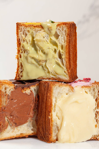 Pyramida ze tří polovin světlých, vločkovitých a jemných croissantů v kostkách s pistáciovou smetanou, vanilkovým pudinkem a čokoládovou náplní. Lahodné sladké francouzské pečivo - Fotografie, Obrázek