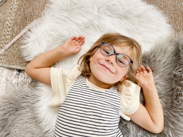 Porträt eines niedlichen Vorschulmädchens mit Brille im Haus. Glückliches lustiges Kind mit neuer blauer Brille - Foto, Bild