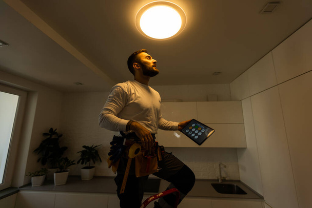 Installation lighting. Builder is holding a tablet in his hands. Concept - lighting engineer. Process installing. Electrician. - Φωτογραφία, εικόνα