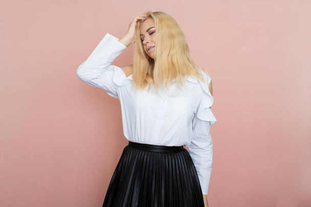 Beauty, fashion portrait. Elegant business style. Portrait of a beautiful blonde woman in white blouse and black skirt posing at studio on a pink background. - Valokuva, kuva