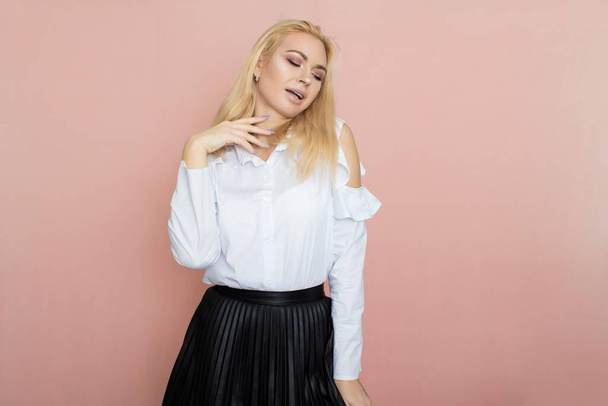 Beauty, fashion portrait. Elegant business style. Portrait of a beautiful blonde woman in white blouse and black skirt posing at studio on a pink background. - Fotoğraf, Görsel