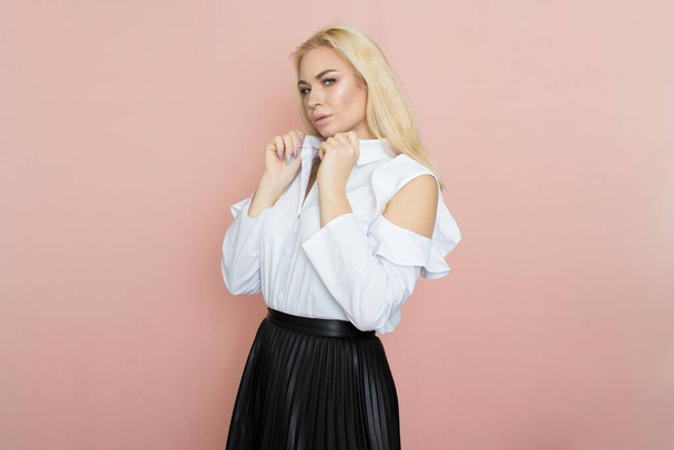Beauty, fashion portrait. Elegant business style. Portrait of a beautiful blonde woman in white blouse and black skirt posing at studio on a pink background. - Фото, изображение