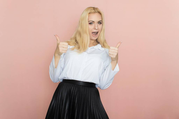 Beauty, fashion portrait. Elegant business style. Portrait of a beautiful blonde woman in white blouse and black skirt posing at studio on a pink background. - Photo, image