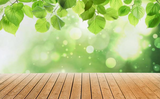 Empty wooden surface and beautiful green leaves on blurred background. Bokeh effect - Fotó, kép