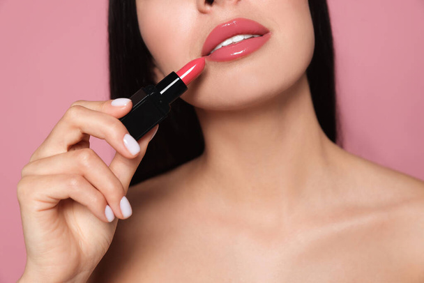 Young woman with beautiful makeup holding glossy lipstick on pink background, closeup - Foto, Bild