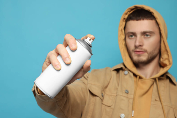 Handsome man holding white spray paint against light blue background - Photo, Image