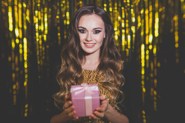 Atraktivní žena s růžovým dárkem dárek box na zlatém pozadí - Fotografie, Obrázek
