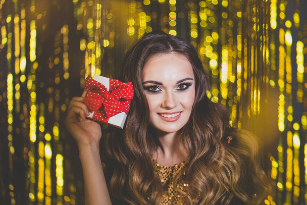 Щаслива красива жінка брюнетка тримає подарункову коробку на золотому фоні боке
 - Фото, зображення