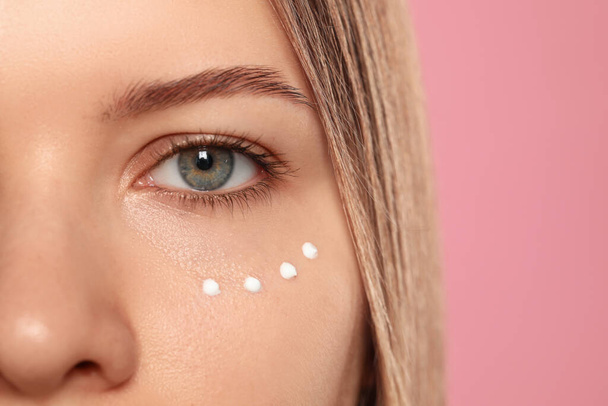 Young woman with cream around eye on pink background, closeup. Space for text - Foto, immagini