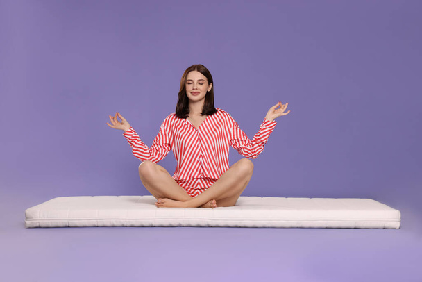 Young woman meditating on soft mattress against light purple background - Фото, зображення