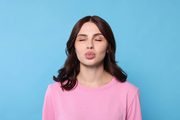 Beautiful young woman giving kiss on light blue background - Foto, Imagen