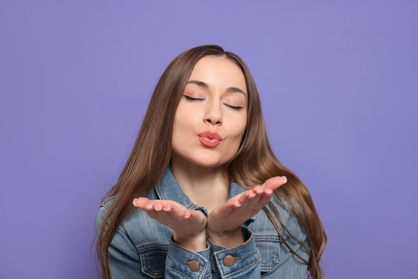 Beautiful young woman blowing kiss on purple background - Фото, изображение