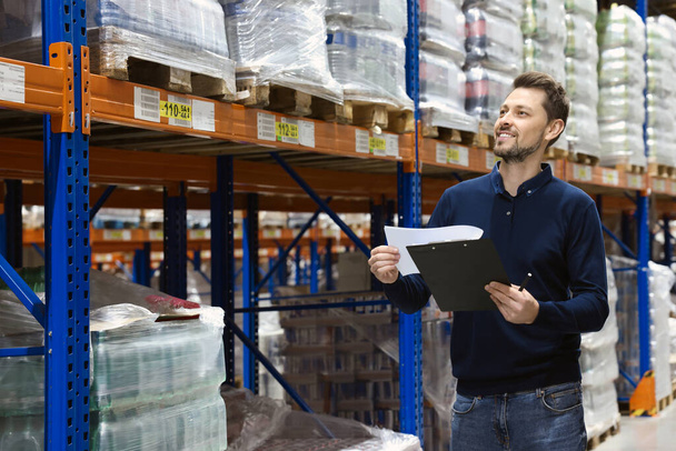 Happy manager holding clipboard in warehouse with lots of products - Foto, Bild