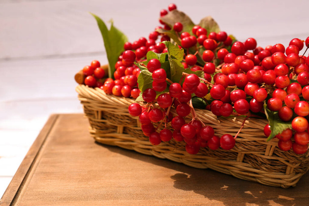 Wicker basket with ripe red viburnum berries on table, closeup - Фото, изображение