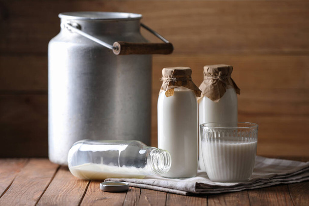 Tasty fresh milk in can, bottles and glass on wooden table - Foto, immagini