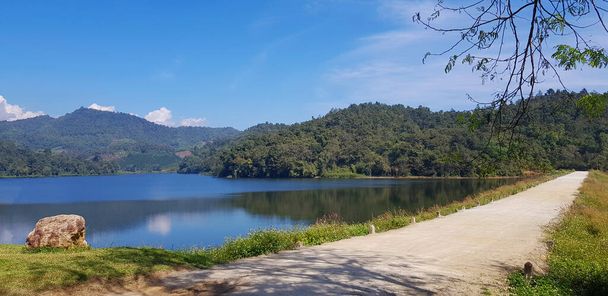 Carretera o calle junto al lago o río con montaña verde y fondo azul en el embalse Huai Bon Chiang Mai, Tailandia. Entre la naturaleza con reflexión sobre el agua y el espacio de copia. Belleza en la naturaleza  - Foto, imagen