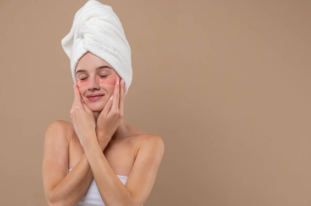Beauty procedures. Young girl with towel on head and with patches under eyes - Valokuva, kuva