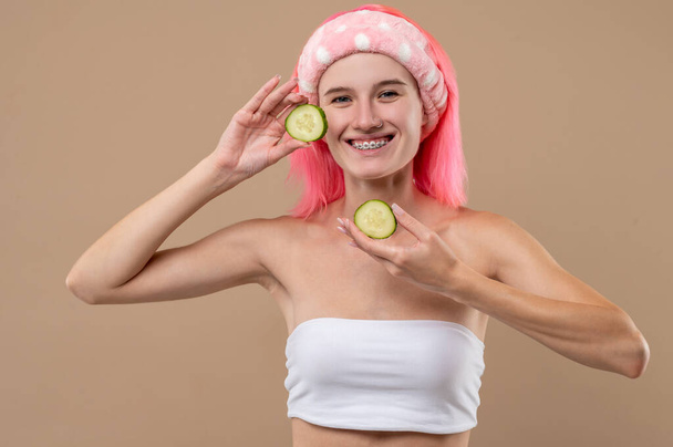 Естественная косметика. Розововолосая девушка с кусками огурца в руках - Фото, изображение