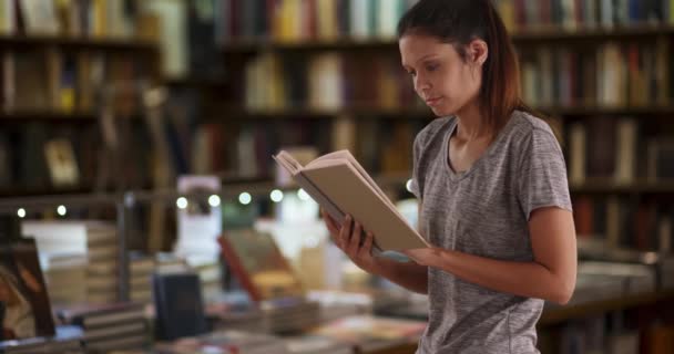 Gyönyörű fiatal nő olvas a könyvtárban. Vonzó női hallgató tanul az egyetemi könyvtárban. 4k - Felvétel, videó