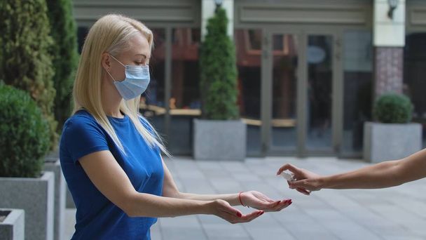 Spraying alcohol antiseptic on the hands of a young woman. Blonde in blue blouse treating hands with a bactericidal agent on street background. Preventive measures for COVID-19 during the outbreak - Valokuva, kuva
