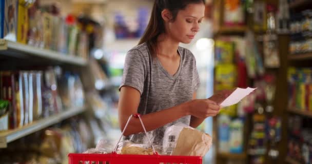 Cliente muito feminino carregando cesta de supermercado à procura de item. Retrato de jovem esposa ou mãe verificando sua lista de compras. 4k - Filmagem, Vídeo