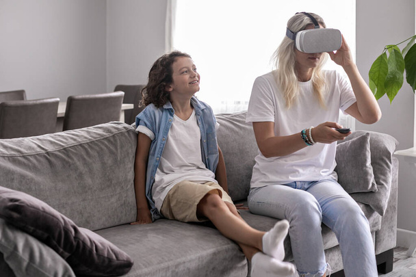 αγόρι παιδί με μητέρα φορώντας ακουστικά εικονικής πραγματικότητας vr γυαλιά στο σαλόνι στο σπίτι έχοντας διασκέδαση που τέμνονται με εικονική πραγματικότητα παίζοντας παιχνίδια - Φωτογραφία, εικόνα