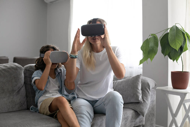Madre e figlio indossano occhiali vr realtà virtuale in salotto a casa divertendosi interagendo con la realtà virtuale giocando - Foto, immagini