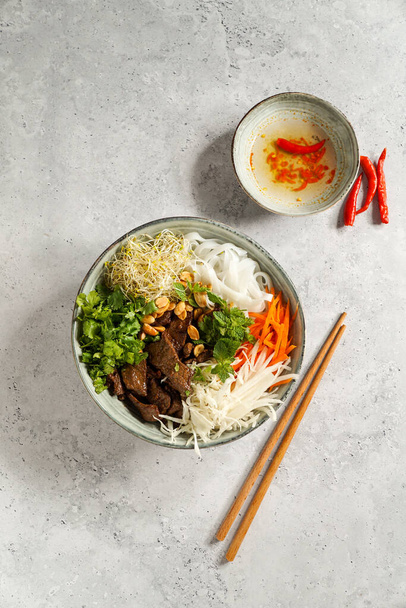 μπολ με παραδοσιακή βιετναμέζικη σαλάτα - Bun Bo Nam Bo, με μοσχάρι, χυλοπίτες ρυζιού, φρέσκα βότανα, λαχανικά τουρσί και σάλτσα ψαριού - Φωτογραφία, εικόνα