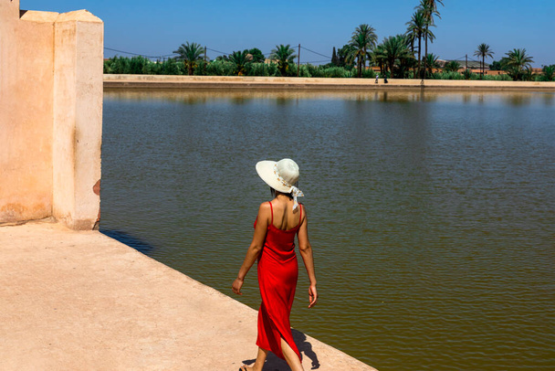 Счастливая женщина прогуливаясь у озера Альменара сады, где крепость отражается в арабском городе Марракеш, одном из самых посещаемых и посещаемых мест в Марокко. - Фото, изображение