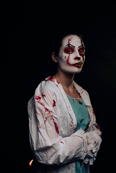 若い女性は顔に恐怖の傷と暗い背景に血の服を持つ流血のゾンビを描きます.ハロウィンの怖いイメージ. - 写真・画像