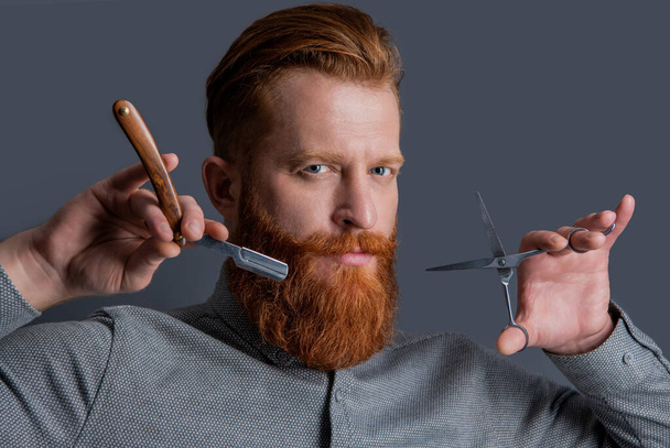 face of man with barber hairstyle. barber man has hairstyle in studio. barber man hold scissors. concept of male hairstyle. man barber with modern hairstyle isolated on grey background. - Foto, Bild