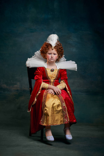 Portrait of little red-headed girl in costume of royal person isolated on dark green background. Queen Elizabeth I. Concept of historical remake, comparison of eras, medieval fashion, emotions, queen - Photo, image