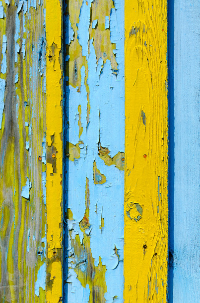 Fragment of wooden fence with cracked yellow and blue paint - Foto, afbeelding