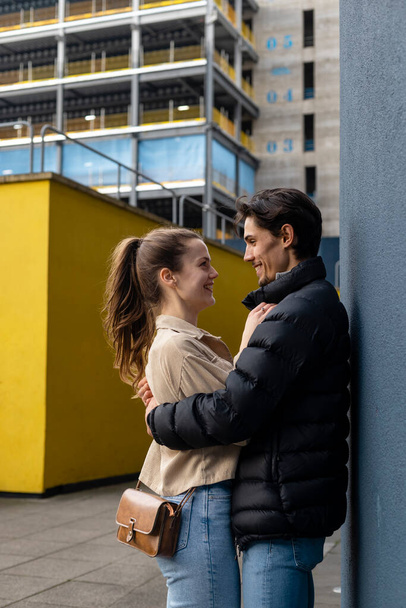 Una foto de vista lateral de una joven pareja de pie cara a cara contra una pared, se abrazan y están enamorados. - Foto, Imagen