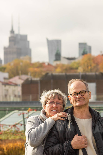 Happy senior couple tourists hugging and walking on the city street of autumn Warsaw. Smiling elderly married in glasses traveling in Europe. Active seniors concept. Happy weekends together.  - Fotoğraf, Görsel