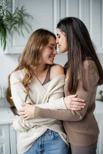 Young lesbian woman hugging partner in sweater in kitchen  - Fotoğraf, Görsel