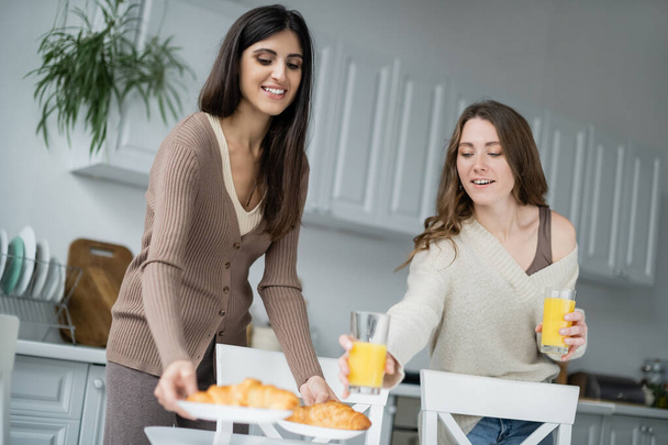 Lesbian women putting orange juice and croissants in kitchen  - 写真・画像