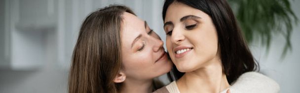 Lesbian woman hugging and kissing partner at home, banner  - 写真・画像