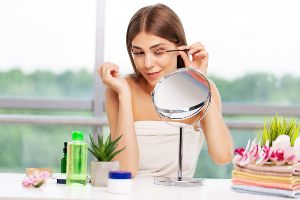vrouw doen ochtend make-up routine zetten mascara in badkamer spiegel thuis. - Foto, afbeelding