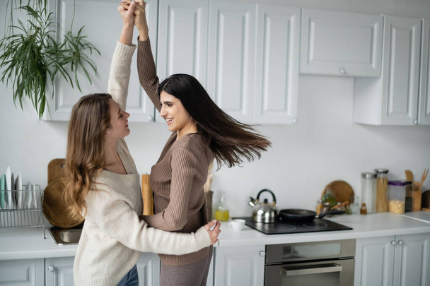 Positive lesbian couple dancing in kitchen at home  - Photo, image