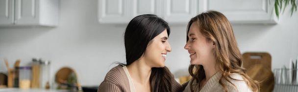 Side view of positive lesbian couple looking at each other in kitchen, banner  - Fotografie, Obrázek